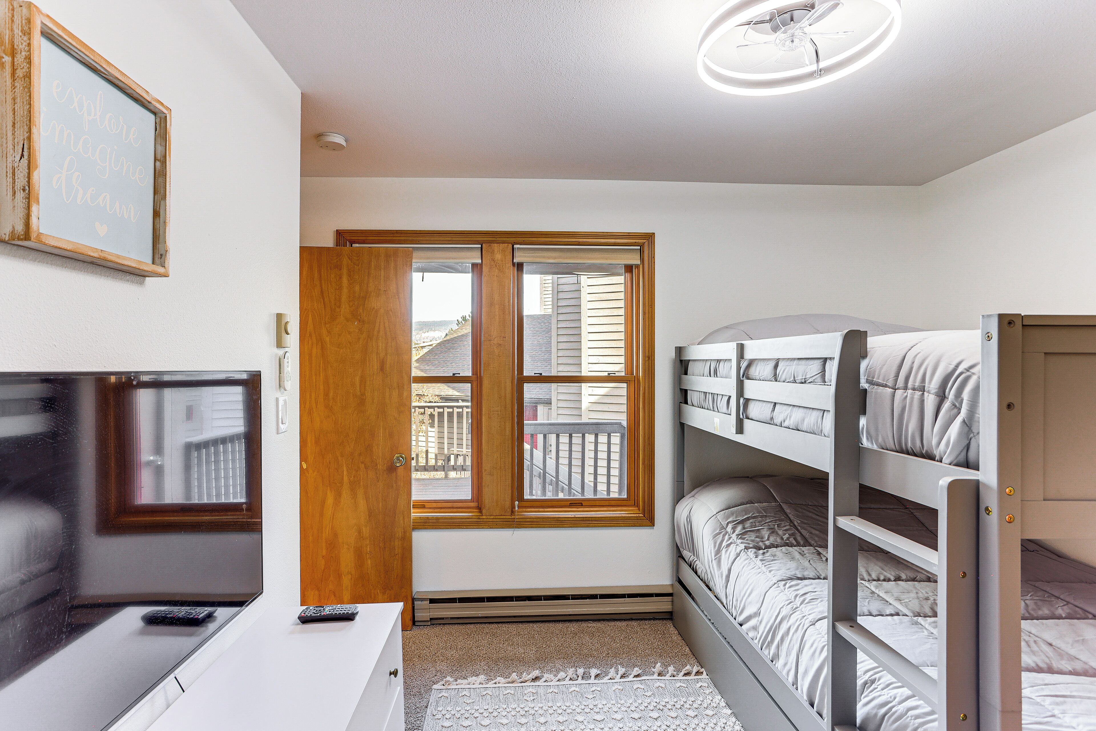 A bedroom with bunk beds, a desk with a computer, and a window with a view of the outside.