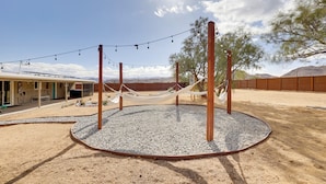 A circular outdoor seating area with a hammock, surrounded by a gravel circle and wooden posts, with a building in the background. - Mtn-view Home w/ Hot Tub: 8 Mi to Joshua Tree! (Joshua Tree)