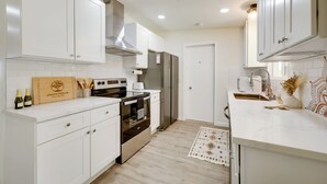A modern kitchen with white cabinetry, stainless steel appliances, and a wooden cutting board with a logo. - Mtn-view Home w/ Hot Tub: 8 Mi to Joshua Tree! (Joshua Tree)