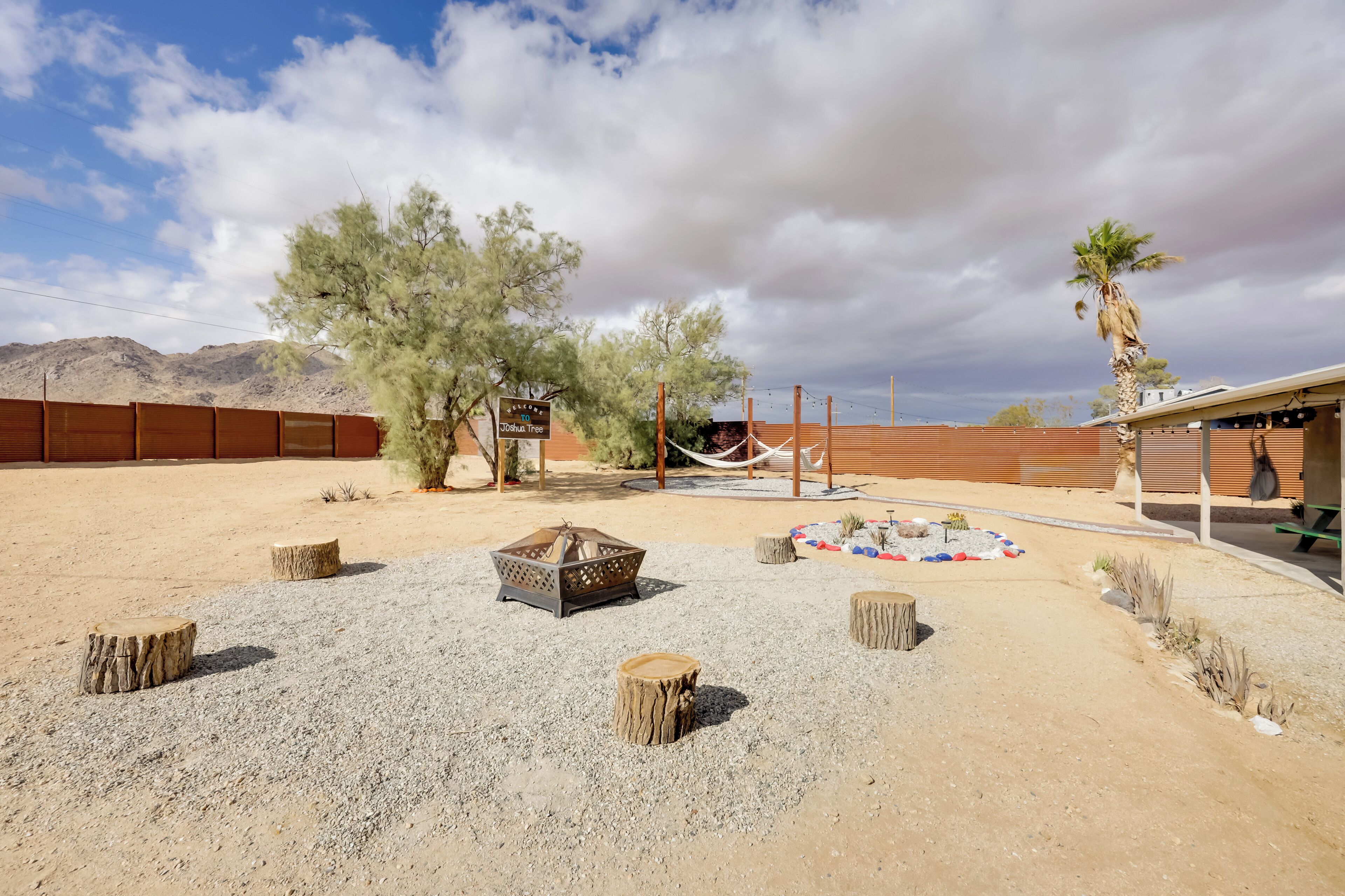 A desert landscape with a fire pit, wooden stumps, and a hammock.