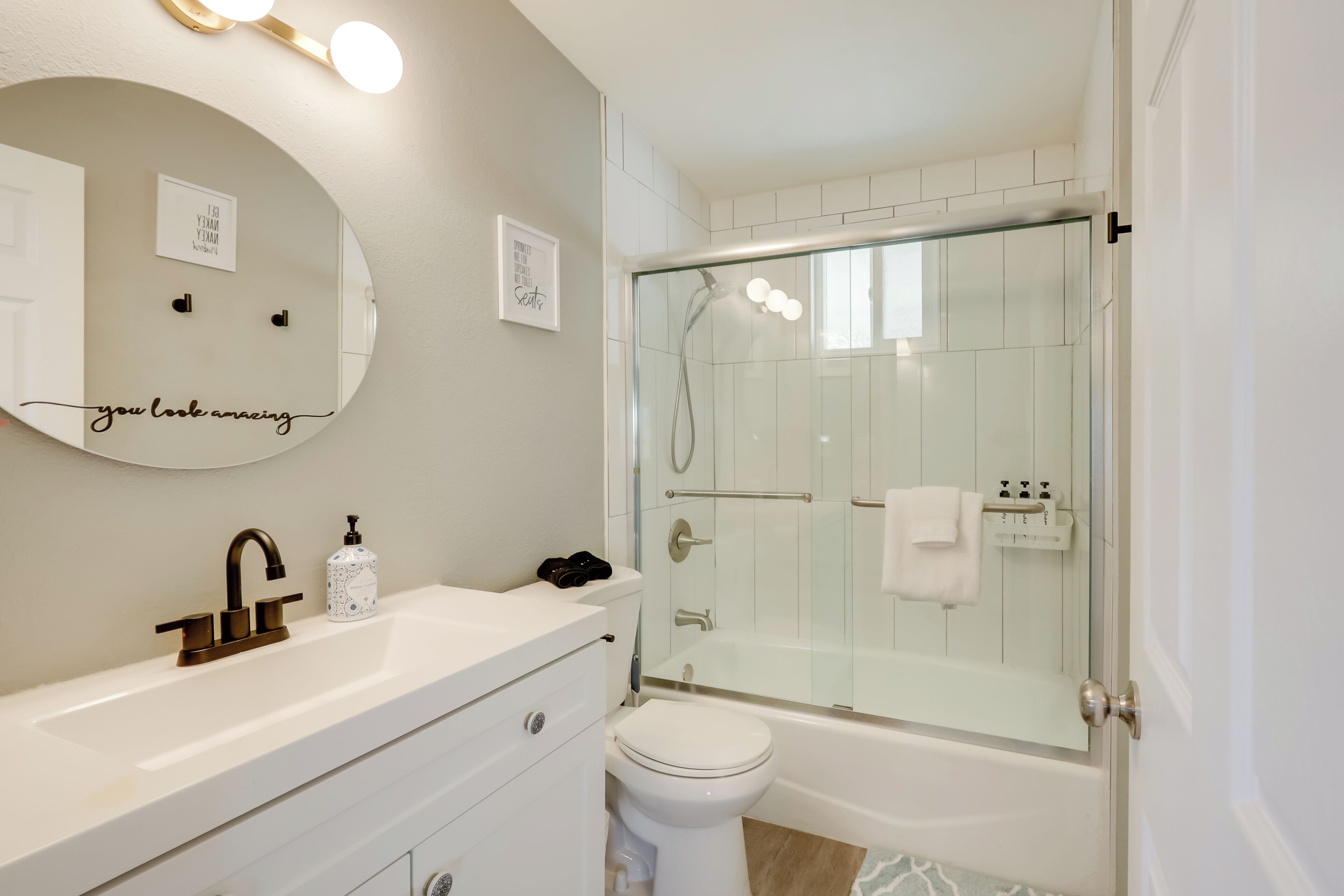 A modern bathroom with a round mirror, a white sink, a toilet, and a glass-enclosed shower area.