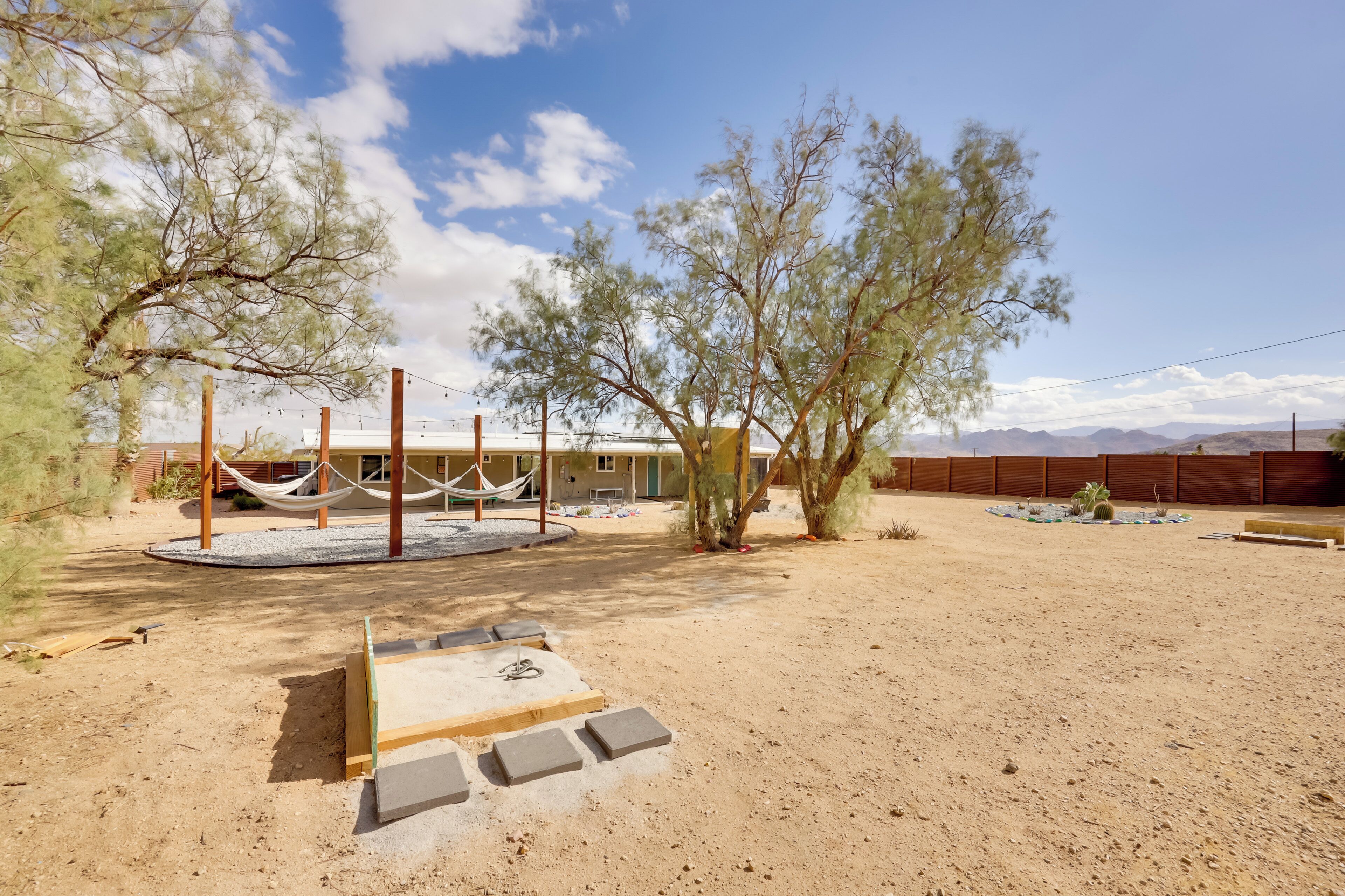A desert landscape with a building, hammocks, and a sandbox.