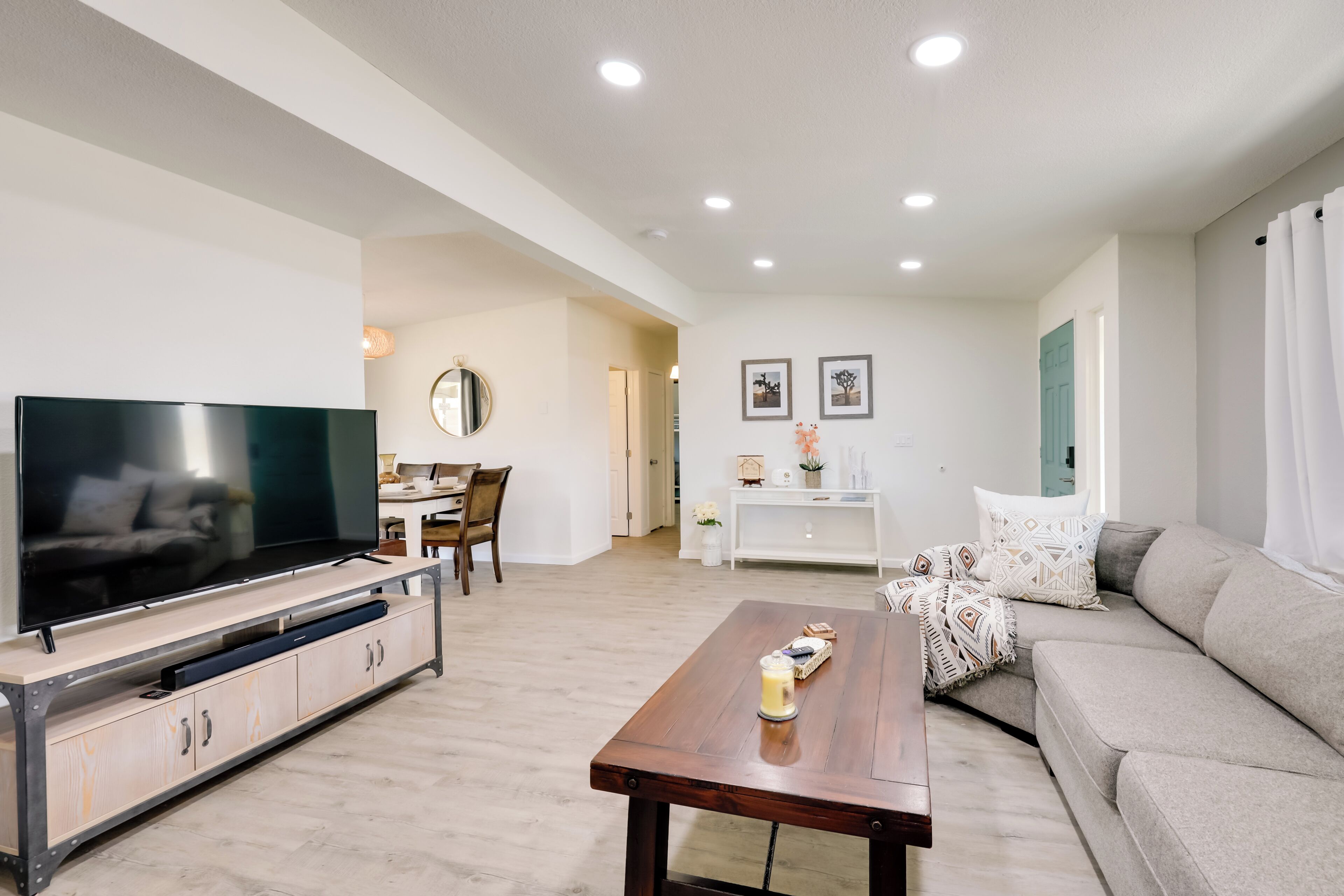 A modern living room with a flat-screen TV, wooden coffee table, and a grey sofa.