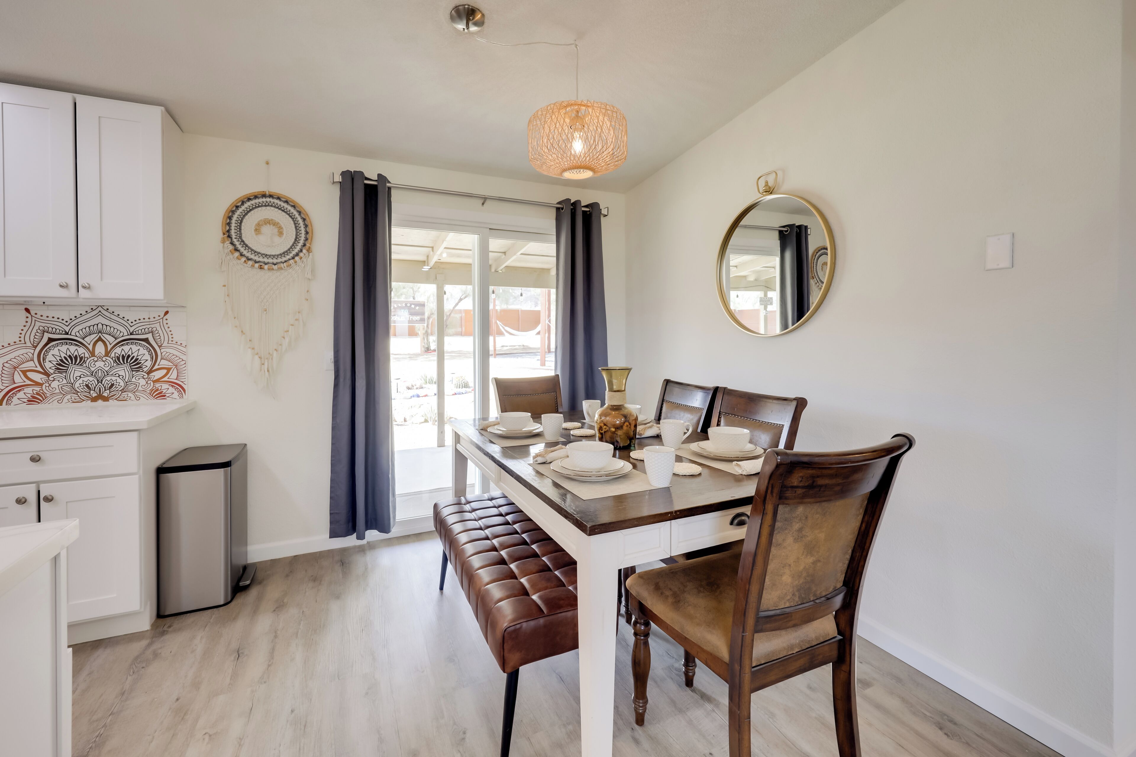 Een eethoek met een tafel voor vier personen, een bank, een prullenbak en een spiegel aan de muur.
