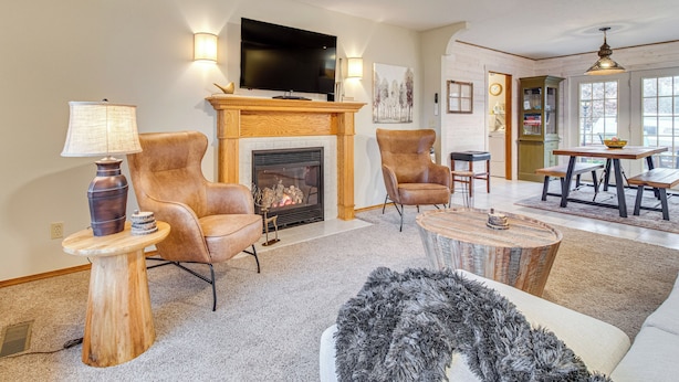 Een woonkamer met een open haard, leren fauteuils, een ronde salontafel en een televisie boven de haard.