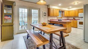 A kitchen with wooden cabinets, a wooden dining table with benches, a hanging light fixture, and a refrigerator. - < 1 Mi to Bull Shoals Lake: 'the Blue Quill' (Bull Shoals)