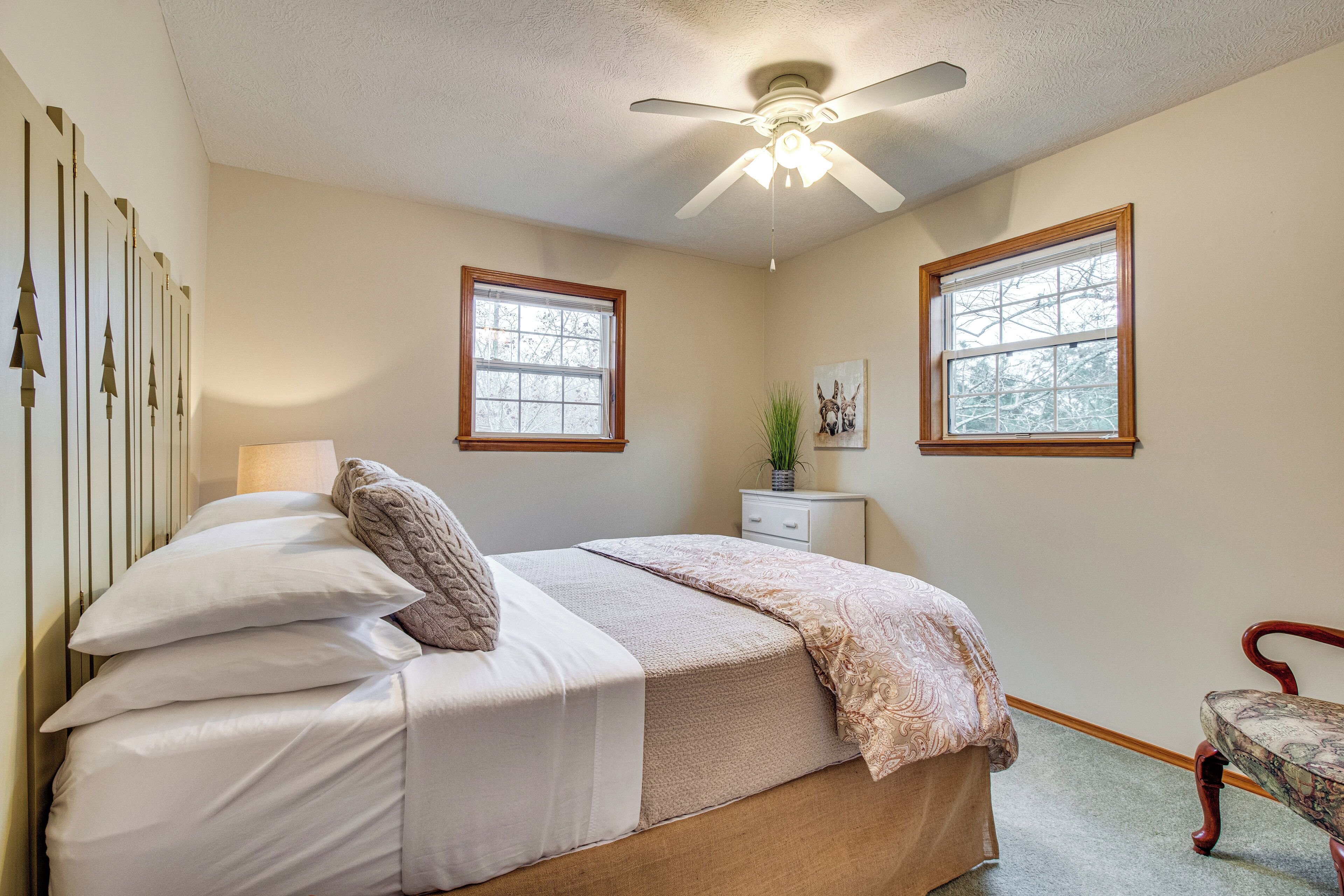 A bedroom with a bed, a nightstand, a chair, two windows, and a ceiling fan.