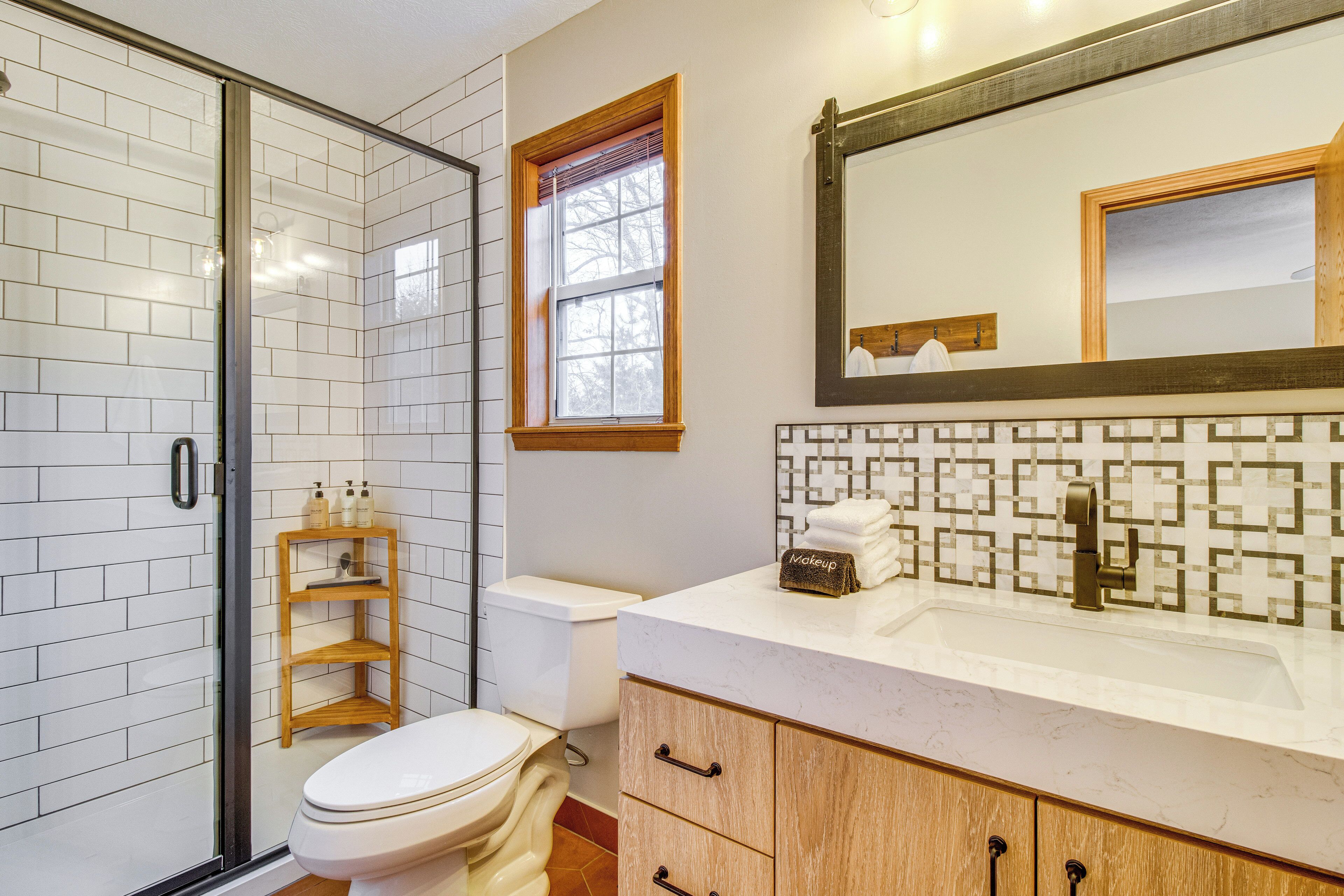 Un baño con cabina de ducha de vidrio, inodoro, tocador con espejo y ventana.