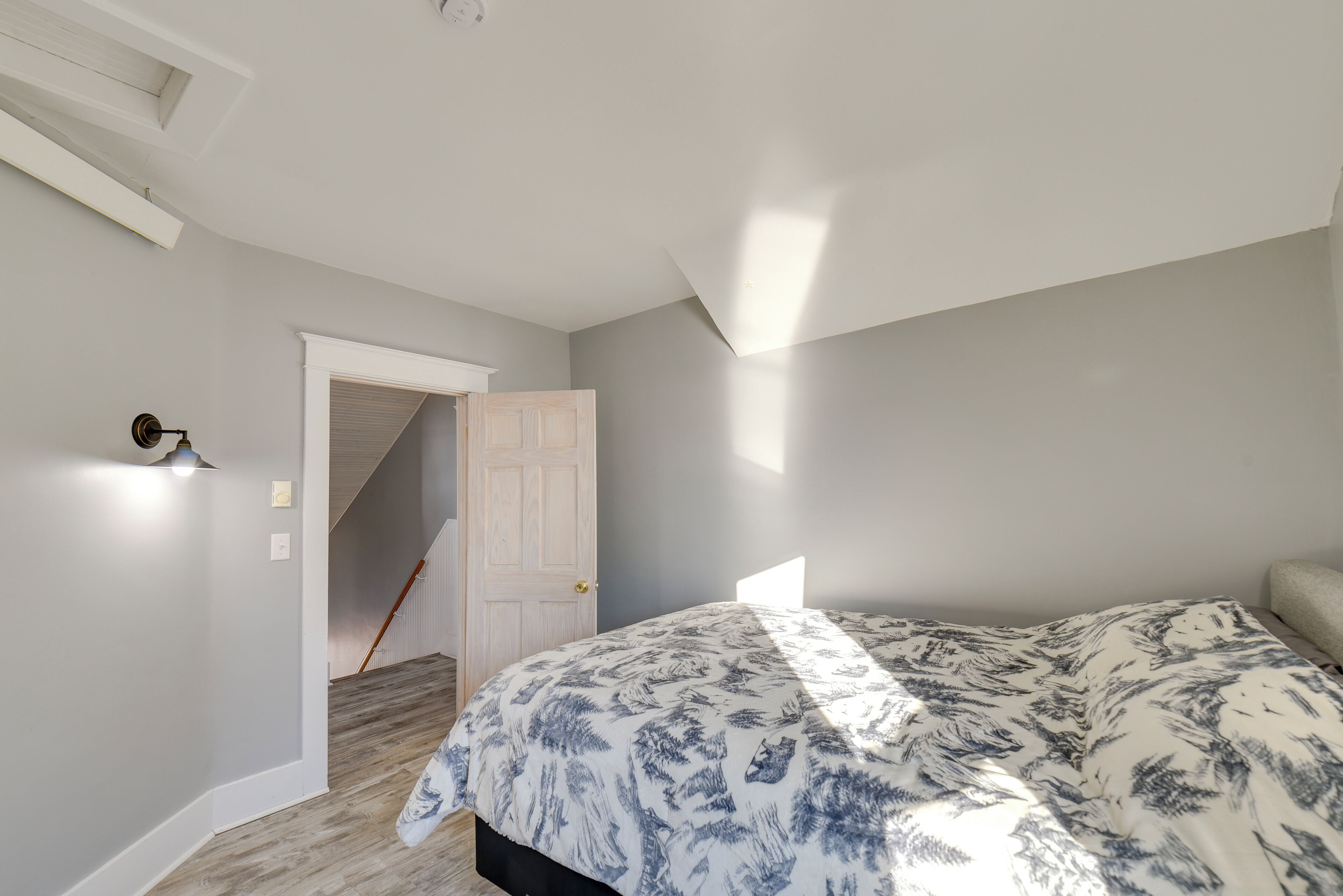 Ein Schlafzimmer mit einem Bett, einer Tür zu einer Treppe und einer Wandleuchte.
