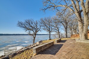 Un sendero de piedra a la orilla de un lago, con árboles desnudos y un cielo despejado.
