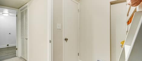 Un pasillo con una puerta cerrada, un cubo de basura y una vista parcial de una cama.