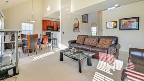 A spacious living room with a leather sofa, a glass coffee table, and a dining area with wooden chairs and a kitchen in the background. - 6 Mi to Charlotte Motor Speedway: Home w/ Fire Pit (Concord)