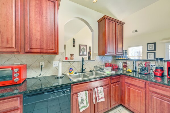 A kitchen with wooden cabinets, a dishwasher, a red toaster, a sink, and various kitchen appliances.