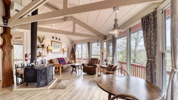 A spacious living room with a wooden dining table, comfortable seating, and large windows offering a view of the outdoors. - BW-7  Mountain Treehouse Authentic Roundhouse (Beech Mountain)