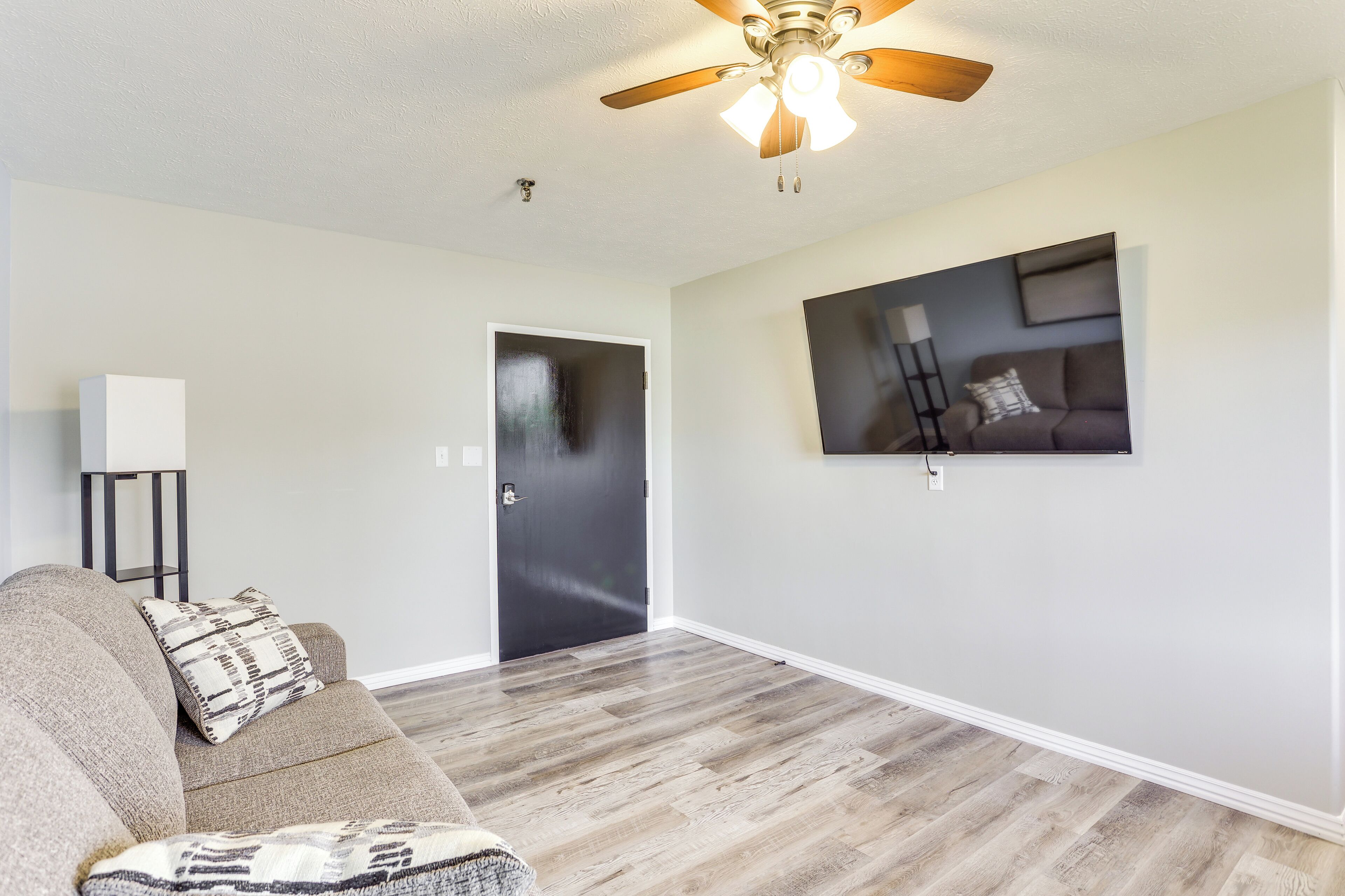 A living room with a sofa, a ceiling fan, a door, and a wall-mounted TV.