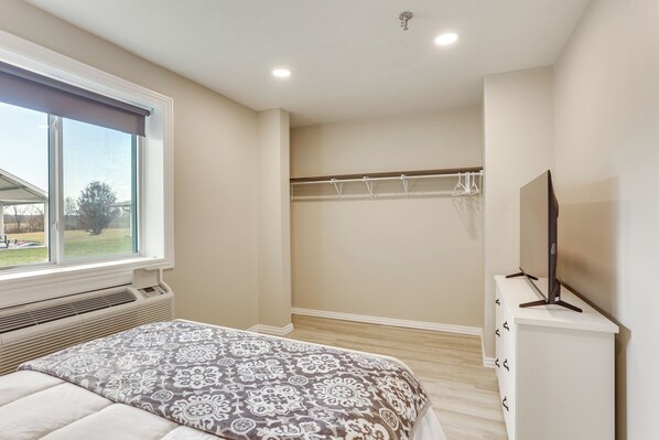 Un dormitorio con cama, ventana, perchero y televisor sobre un mueble.