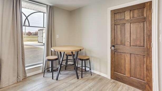 A room with a wooden door, a round table with stools, a window with curtains, and a view of a building outside. - < 1 Mi to Oakland City University: Cozy Apartment (Oakland City)