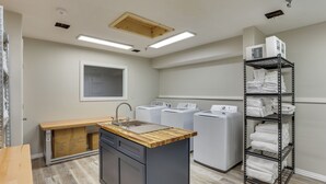 A laundry room with a sink, washing machines, and a metal shelf with folded towels. - < 1 Mi to Oakland City University: Cozy Apartment (Oakland City)
