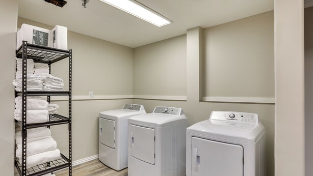 A laundry room with two front-loading washing machines and a metal shelf with folded towels. - Walk to Ocu, Golf: Updated Oakland City Studio! (Oakland City)