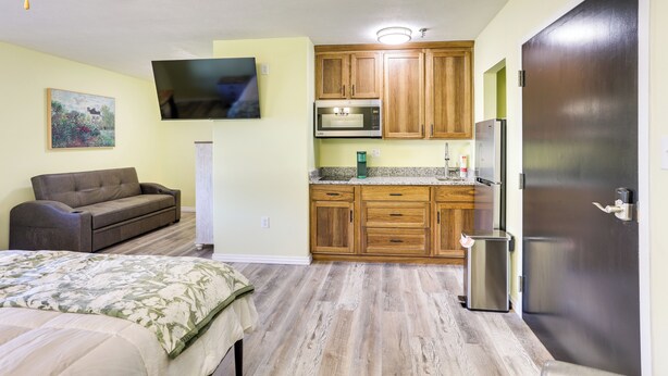 A compact room with a bed, a sofa, a kitchenette with wooden cabinets, a microwave, a refrigerator, and a ceiling fan. - Quiet Oakland City Studio: Walk Downtown! (Oakland City)
