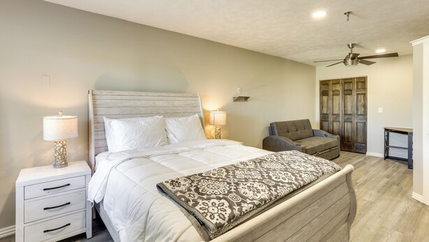 Une chambre à coucher comprenant un lit, des tables de chevet, une chaise, un ventilateur de plafond et une armoire.