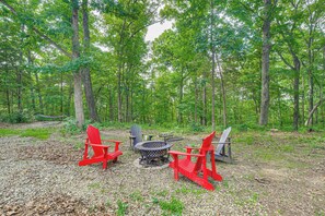 A forested area with a fire pit and red Adirondack chairs. - Home w/ Trail Access on 19 Acres in Wright City! (Wright City)