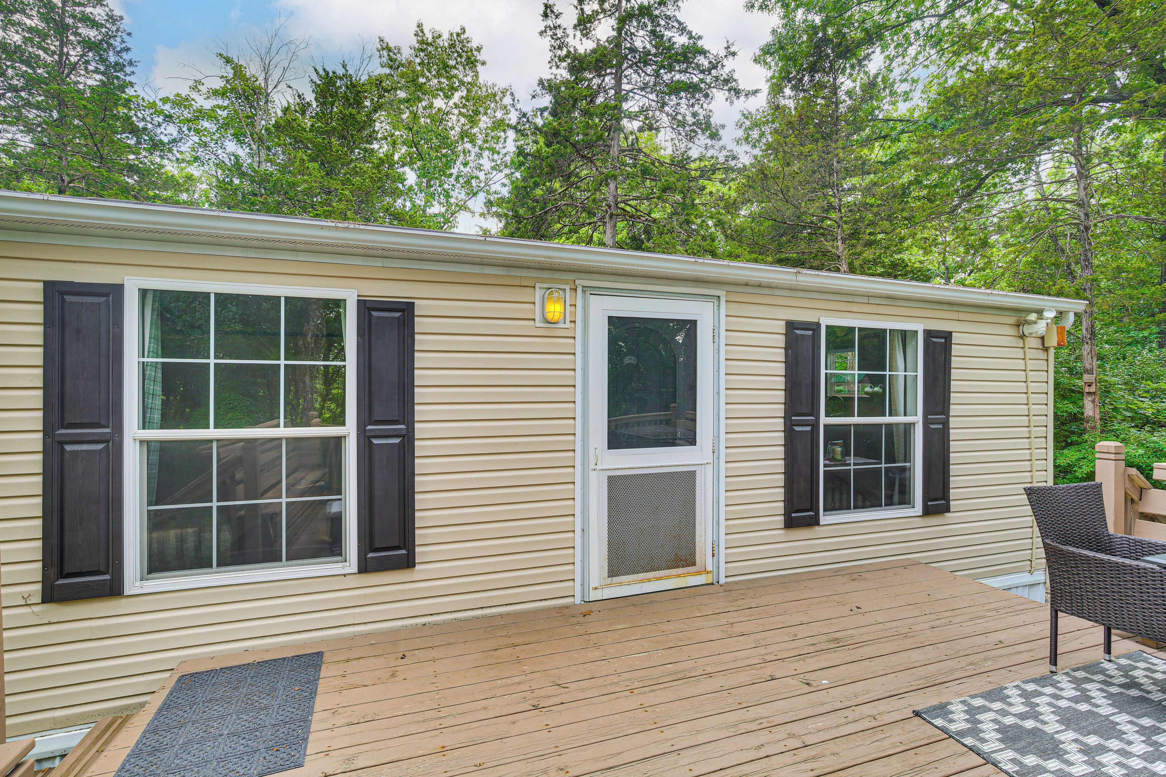 A single-story mobile home with a deck, a covered porch, and a door with a screen.