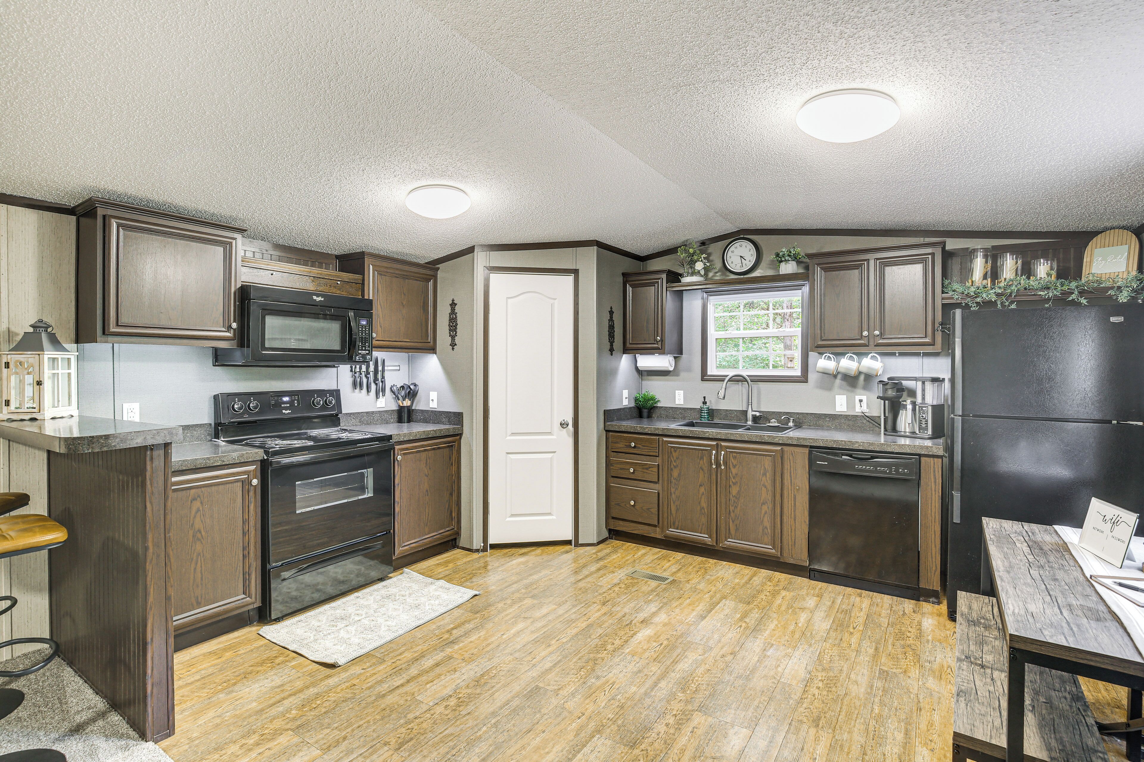 A kitchen with wooden cabinets, a black refrigerator, a microwave, an oven, and a sink.