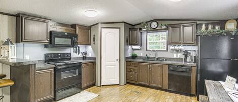 A kitchen with wooden cabinets, a black refrigerator, a microwave, an oven, and a sink.