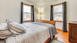 Un dormitorio con cama, mesita de noche y ventana con cortinas.
