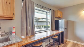 A kitchen with a wooden countertop, two bar stools, a refrigerator, and a window with curtains.