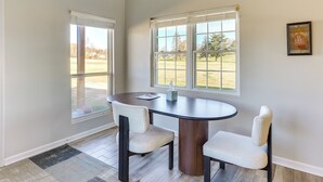 A dining area with a round table and two chairs, large windows with blinds, and a framed family rules poster on the wall. - Golf Course Views: Oakland City Retreat (Oakland City)
