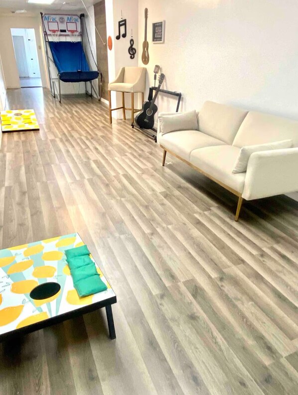 Una sala de estar con piso de madera, un sofá blanco, una mesita con un cojín verde, un tobogán azul y una guitarra apoyada en la pared.