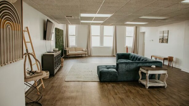 A spacious living room with a large sectional sofa, a flat-screen TV mounted on the wall, and a wooden floor. - Downtown condo Cozy 2-bedroom with plenty of space. (Owensboro)