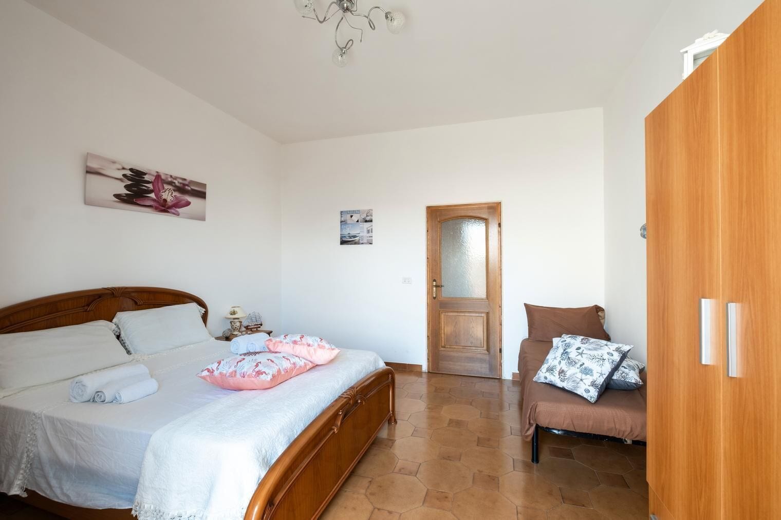 A bedroom with a wooden bed, a wooden wardrobe, a wooden chair, and a door leading to another room.