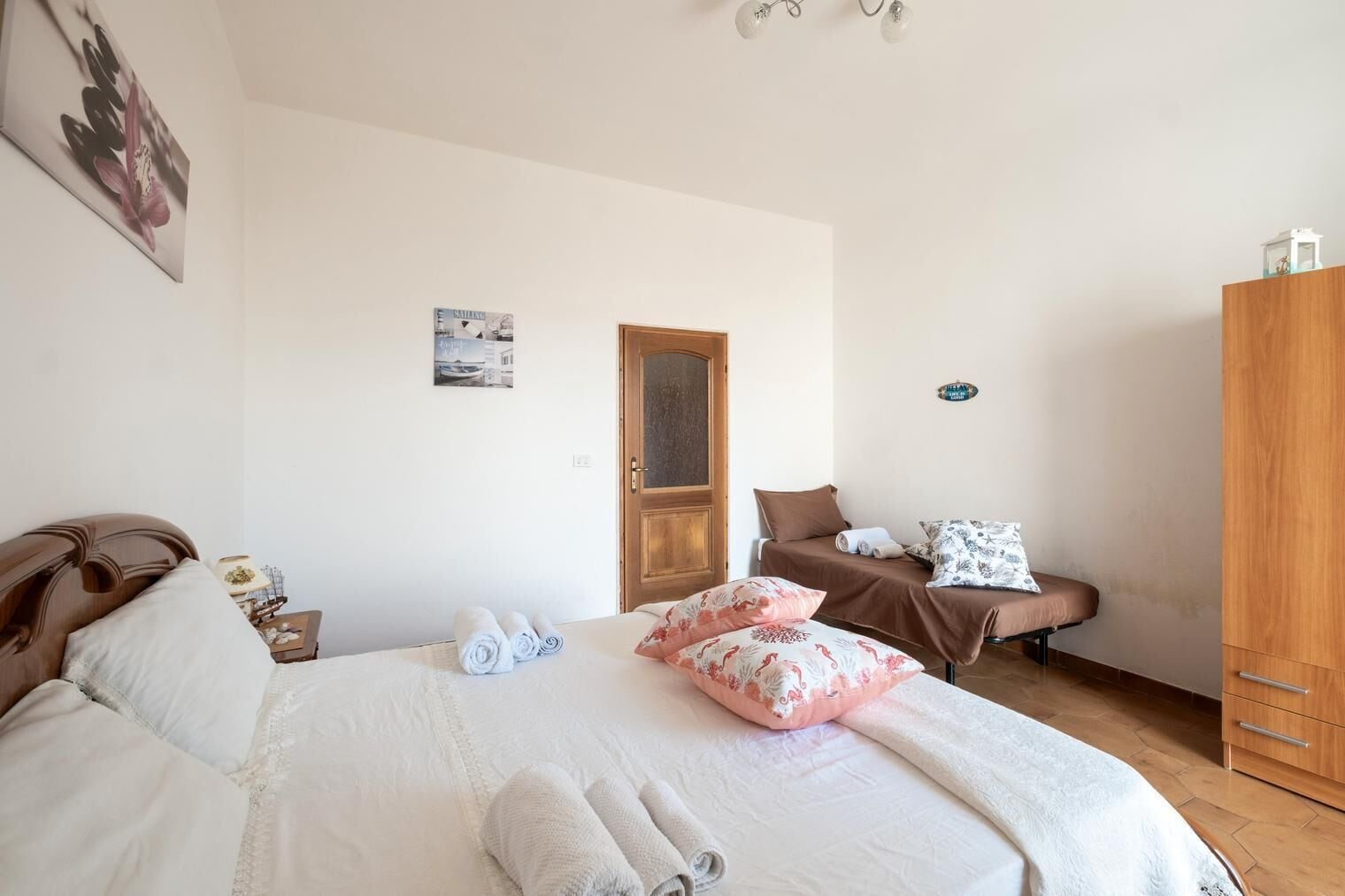 Une chambre avec un grand lit, un plus petit lit, une armoire et une porte.