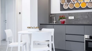 A modern kitchen with white chairs, a dining table, and a variety of spices displayed on the wall. - Appartamento Guglielmo (Oristano)