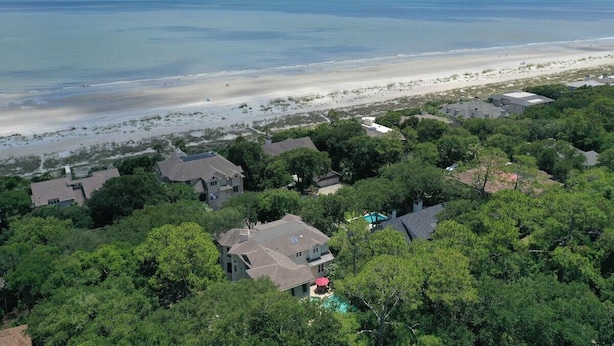 Vue aérienne d’une zone résidentielle côtière, avec des maisons, une plage et un ciel dégagé.