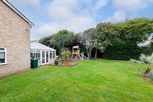 A brick house with a conservatory, a swing set, and a fenced yard.