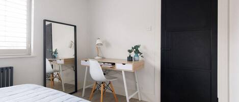 A bedroom with a bed, a desk with a chair, a mirror, and a black door.