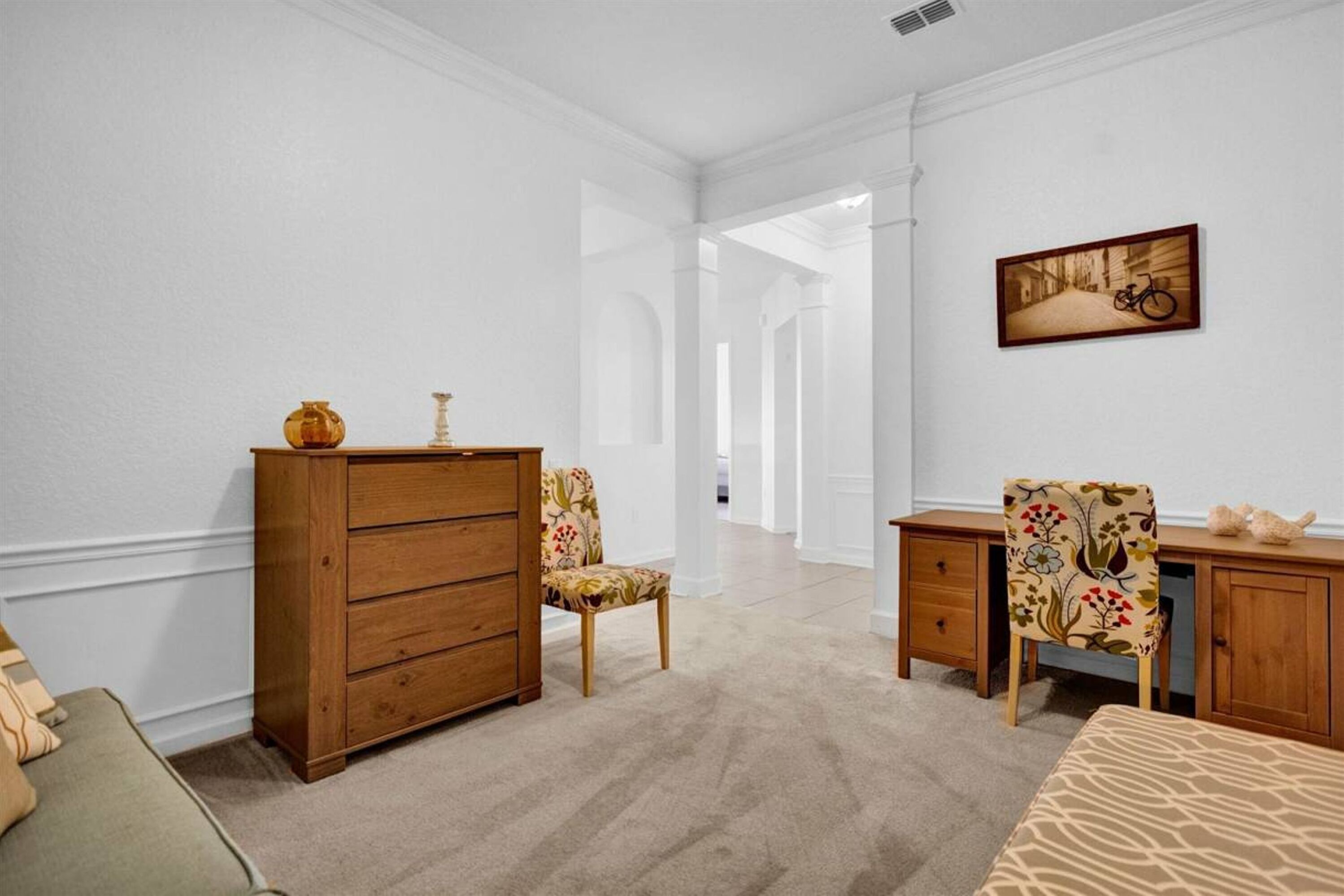 A hotel room with a wooden dresser, a chair with floral upholstery, a desk with a chair, and a bed with patterned bedding.