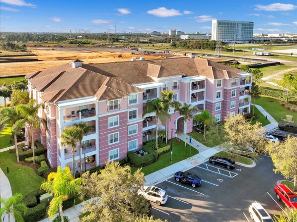 A multi-story hotel with a parking lot, surrounded by greenery and a clear sky.