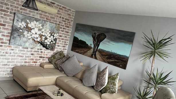 A modern living room with a sectional sofa, a coffee table, and two large paintings on the wall.