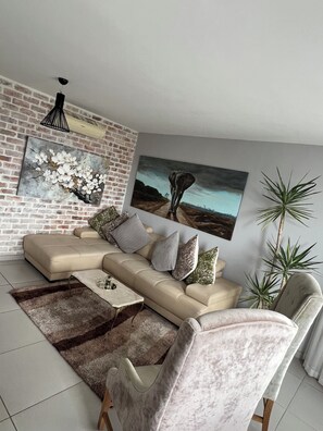 A modern living room with a sectional sofa, a coffee table, and two large paintings on the wall. - Safe and secure Wild olive apartments. 2 minutes walk to the mall and Hospital  (Windhoek)
