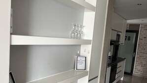 A modern kitchen with white cabinetry, a built-in oven, and a brick accent wall.