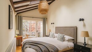 Un dormitorio con una cama grande, un cabecero de madera, una mesita de noche con lámpara y vistas al exterior a través de una puerta corrediza de vidrio.