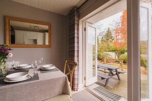 Un comedor con una mesa preparada para dos, un espejo sobre la mesa y vista al patio exterior.
