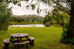 Una mesa de picnic en un área verde, con un río y colinas al fondo.