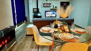 A dining area with a glass table set for four, a fireplace, and a kitchen in the background.