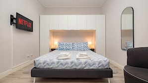 Ein modernes Hotelzimmer mit Bett, Wandfernseher, Spiegel und Sessel.